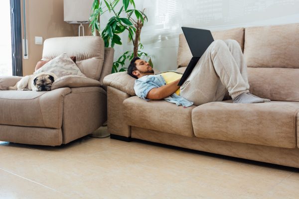 young-man-resting-sofa-home-using-laptop-with-his-dog-beside-him